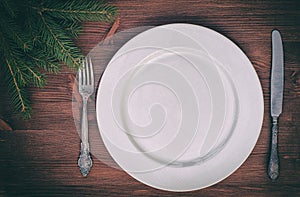 White empty plate with knife and fork on brown wooden surface