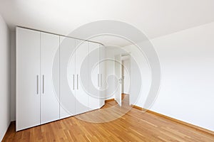 White empty room with large white wardrobe and open door on the corridor