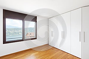 White empty room with windows overlooking the lake and large white wardrobe