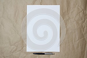 White empty sheet of A4 format with pen on a beige craft paper.