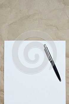 White empty sheet of A4 format with pen on a beige craft paper, vertically oriented.