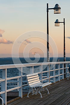 white empty wooden bench on pier by sea or ocean water, tranquility and serenity concept, calm sunset scene
