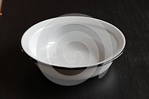 A white enameled empty clean bowl stands on a dark table against a black background