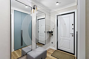 White entrance door in a modern renovated hallway with large mirrors and wardrobe