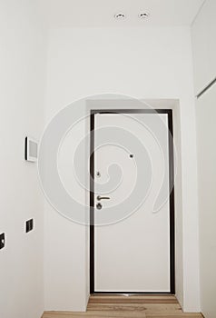 White entrance hall, entryway in a renovated apartment with black and white armored door, a peephole, door handle and door lock,