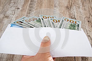 White envelope with dollars in hand on a wooden background.