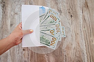 White envelope with dollars in hand on a wooden background.