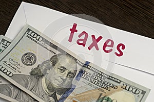 White envelope with the inscription taxes and dollar bills lie on a wooden table. Manage your finances and save money concept.