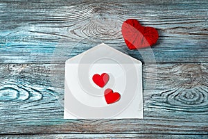 White envelope and red hearts on a blue-gray wooden background.