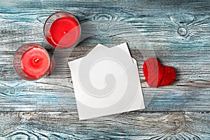 White envelope, red hearts, ribbon and candles on a wooden gray-blue background.