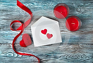 White envelope, red hearts, ribbon and candles on a wooden gray-blue background.