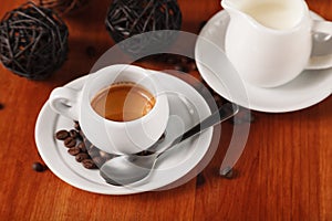 White espresso coffee Cup, coffee beans and milk jug on wooden background. Concept of coffee breaks and serving coffee