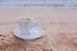 White espresso coffee cup on the sand in the morning day