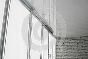 White fabric roller blinds on the plastic window on a balcony in the living room with a reflection in a stretch ceiling.