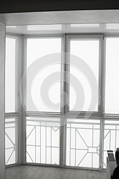 White fabric roller blinds on the plastic window on a balcony in the living room with a reflection in a stretch ceiling.