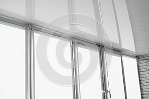 White fabric roller blinds on the plastic window on a balcony in the living room with a reflection in a stretch ceiling.