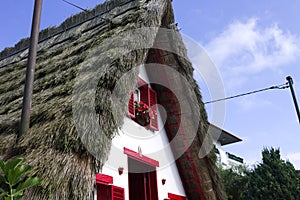 White facade of a traditional house in Santana Madeira with red windows and a thatched roof Portugal