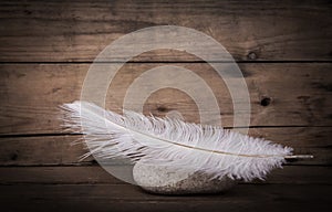 White feather and a stone on wooden dark background for mourning