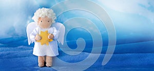 White felt Christmas angel with yellow star in hands on blue silk background,.