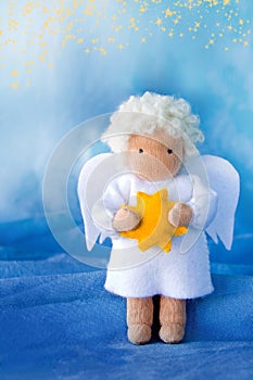 White felt Christmas angel with yellow star in hands on blue silk background,.