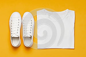 White female fashion sneakers, white T-shirt on yellow orange background. Flat lay top view copy space. Women`s shoes