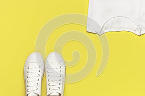 White female fashion sneakers, white T-shirt on yellow orange background. Flat lay top view copy space. Women`s shoes. Stylish