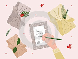 White female hand write greeting card with gift gift furoshiki and green branch, red berries. Eco Christmas and New Year