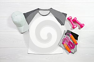 White female sport t shirt mock up flat lay on wooden background. Summer accessories. Sporty trousers, pink female dumbbells. Top