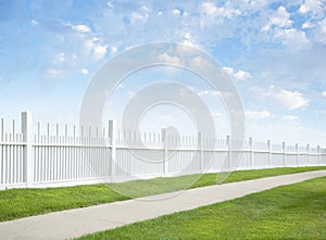 White fence, grass, sidewalk, blue sky and clouds photo