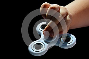 White fidget spinner toy held in left hand of small girl, black background