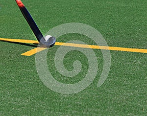 White field hockey ball about to be struckon a green astroturf pitch.