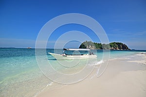 White fine sandy sand & shallow blue water with speed boat & cloudless sky at Pulau Lima Besar island, Johor, Malaysia photo