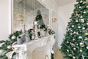 White fireplace decorated with candles and fir branches. Decorated Christmas tree. Classic apartments, morning in hotel