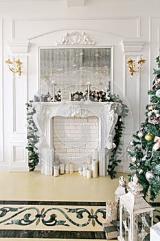 White fireplace decorated with candles and fir branches. Decorated Christmas tree. Classic apartments, morning in hotel