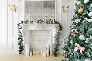 White fireplace decorated with candles and fir branches. Decorated Christmas tree. Classic apartments, morning in hotel