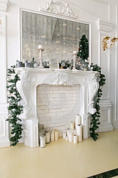 White fireplace decorated with candles and fir branches. Decorated Christmas tree. Classic apartments, morning in hotel