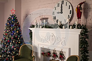 White fireplace with stucco patterns, candles, wach face, fir branches. Christmas decor. Close up. Selective focus