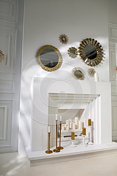 White fireplace in the wall with large candles and round gold mirrors