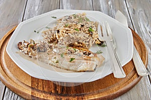 White fish fillet with risotto on plate with fork on wooden background