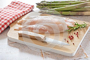 White fish on a wooden board with green asparagus