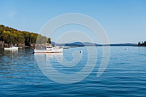 White fishing boats on calm blue water in a harbor surrounded by islands and mountains in fall colors