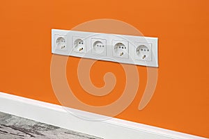 White five-way wall power socket on the orange wall