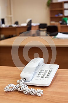 White fixed network telephone stands on office desk, empty room