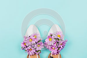 White flat female shoes filled with pink daisies and wildflowers on pastel blue background