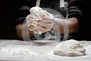 White flour flies in air on black background, pastry chef claps hands and prepares yeast dough for pizza pasta