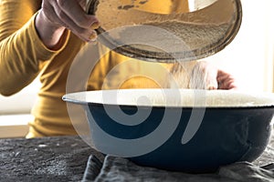 White flour is sieved in a large blue bowl