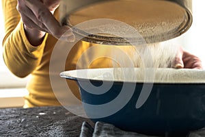 White flour is sieved in a large blue bowl