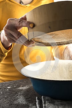 White flour is sieved into a large blue bowl with a free space