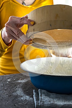 White flour is sieved into a large blue bowl with a free space