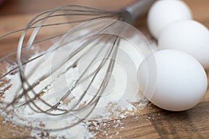 White flour, three eggs and a whisk on a wooden table